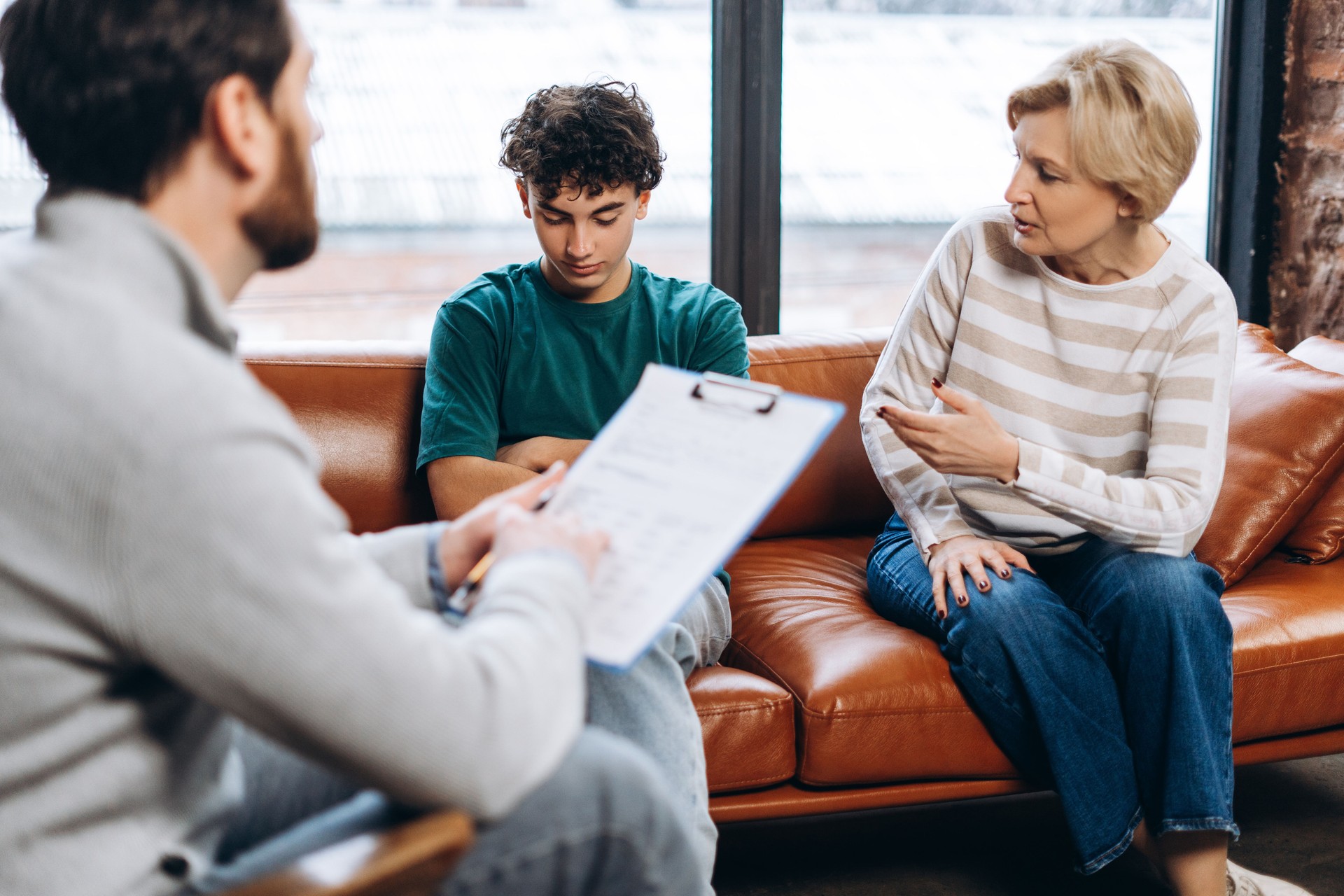 Male psychoanalyst making notes listening mother and her teenager son