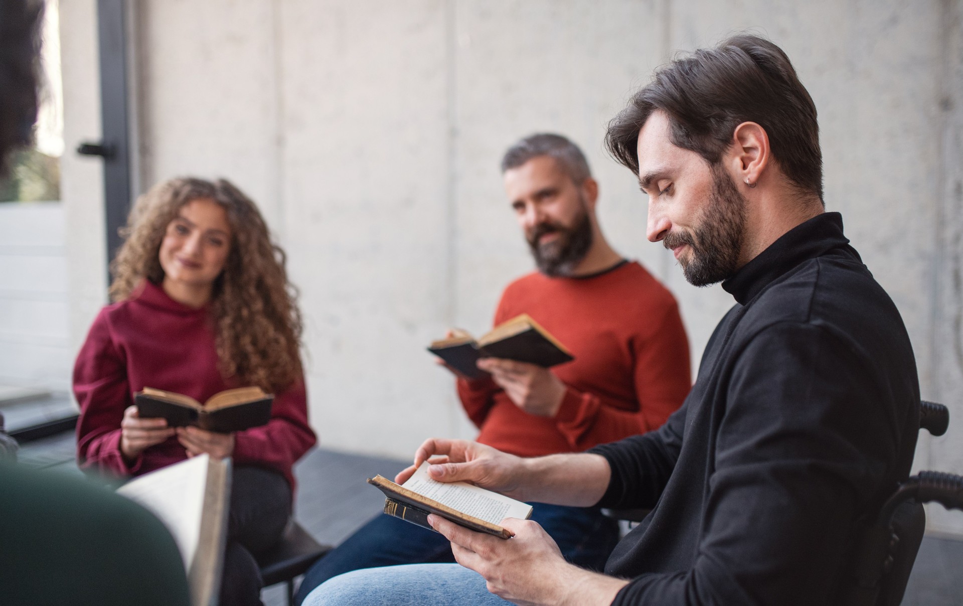 Men and women sitting in circle reading Bible book during group therapy.